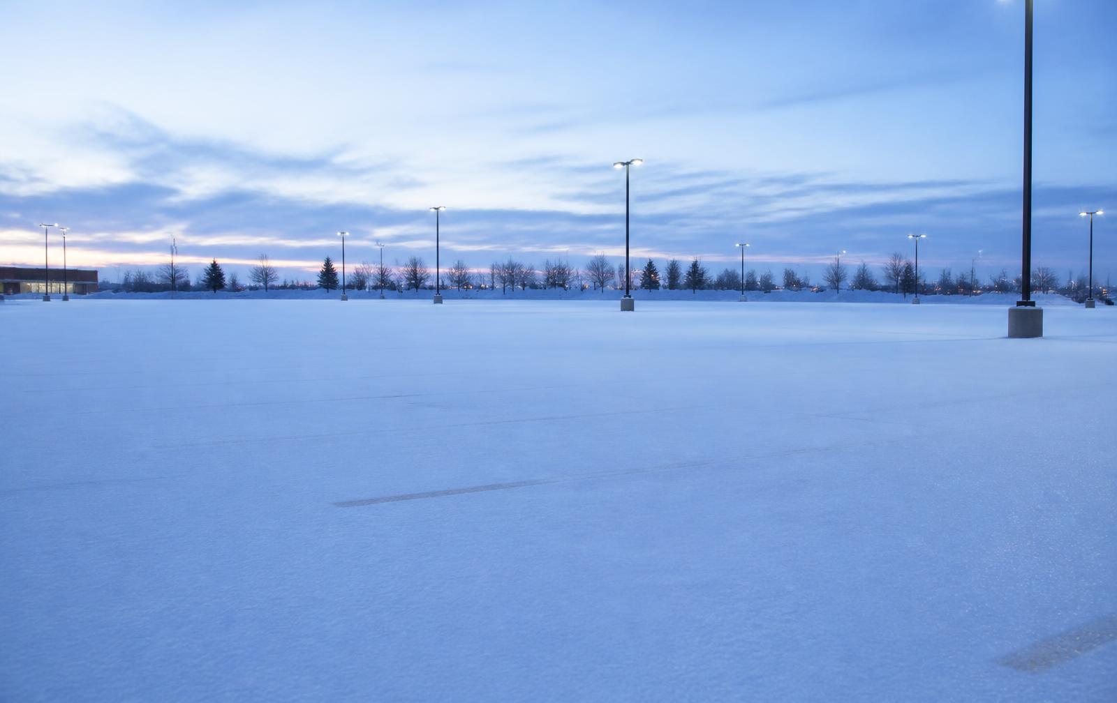 Empty snow-covered commercial parking lot at dawn under cold blue light